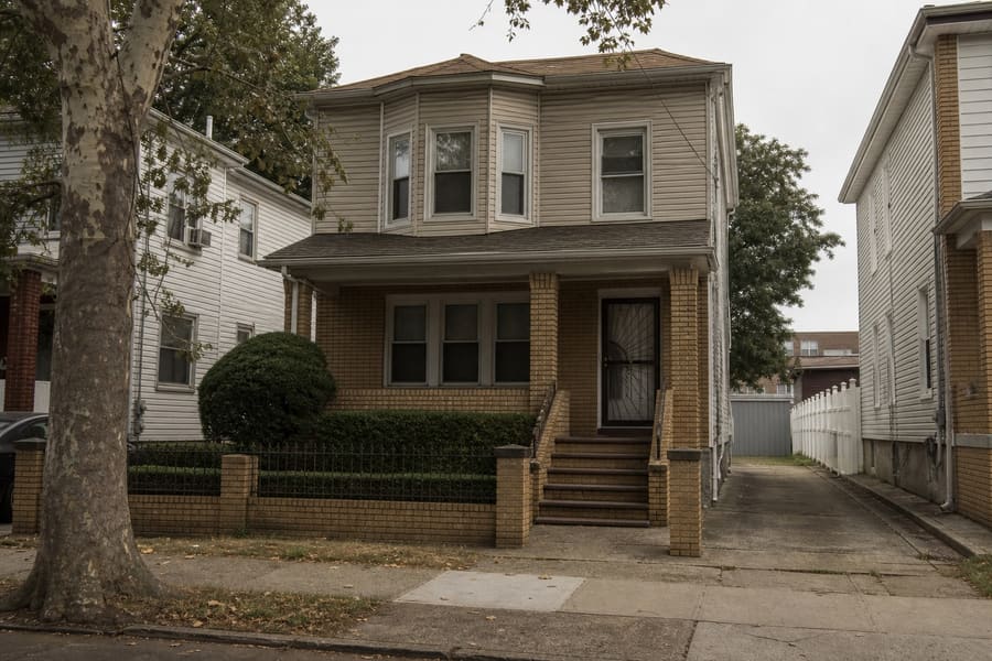 A two family house with brick and siding, steps to the front door and a narrow side driveway