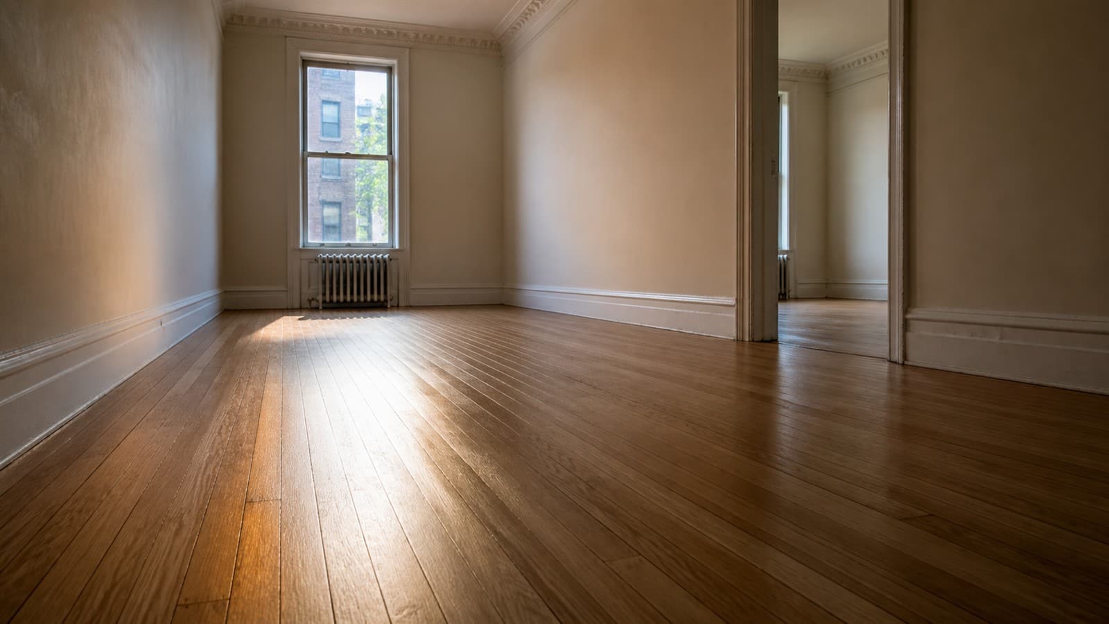 Refinished oak strip flooring running the length of a sunlit room in a Bronx apartment